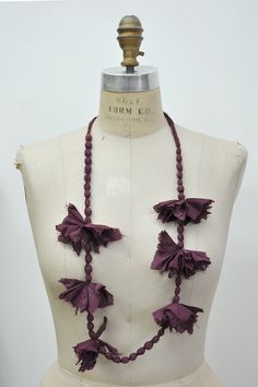 a white mannequin with purple flowers on it's neck and two necklaces