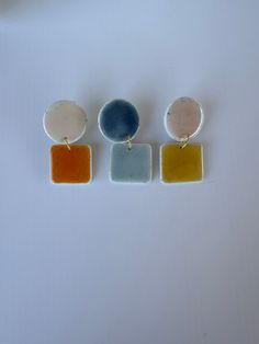 three different colored square shaped earrings on a white surface