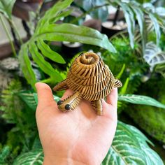 a hand is holding a small animal made out of wicker in front of some plants