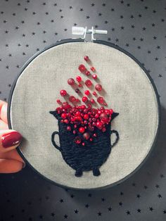 a hand embroidery project with red beads in a black pot on a gray background, surrounded by stars