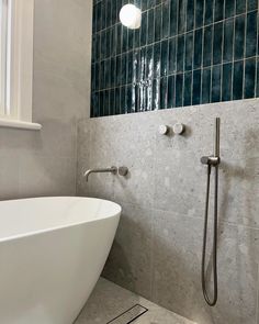 a white bathtub sitting next to a window in a bathroom with blue tile on the walls