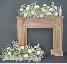 a fireplace with white flowers and greenery on it in front of a gray wall