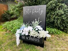 a chalkboard sign with flowers on it in front of some bushes and shrubs that says let's party the normans