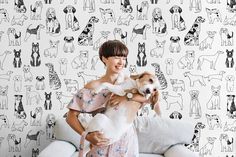 a woman holding two dogs in front of a wall with cats and dogs on it