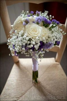 a bridal bouquet sitting on top of a wooden chair with purple and white flowers