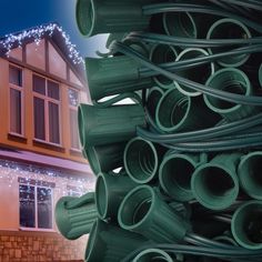 a large stack of green plastic pipes in front of a house with christmas lights on the roof