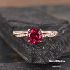 a ring with a red stone in the middle and white diamonds around it on a rock