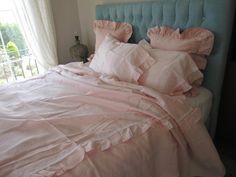 a bed with pink sheets and pillows in a bedroom next to a large window,