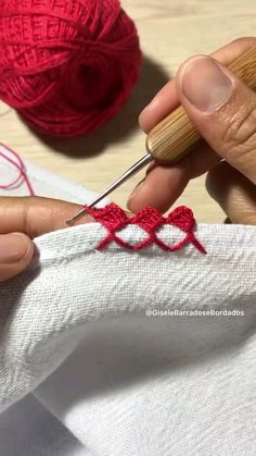 someone is knitting something on a piece of white fabric with red yarn in the background