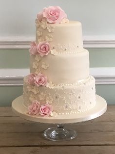 a three tiered wedding cake with pink flowers on top and white icing, sitting on a wooden table