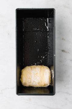 an uncooked loaf of bread in a black box on a marble countertop