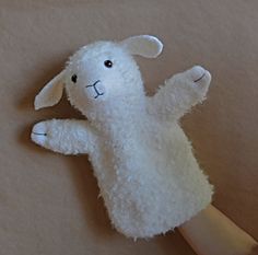 a white stuffed animal laying on top of a wooden table next to a person's hand