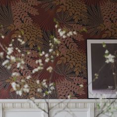 a vase with flowers on top of a shelf in front of a wallpapered wall