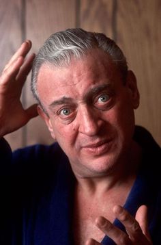 a man with grey hair and blue shirt holding his hand up to his head while looking at the camera