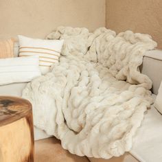 a large white blanket sitting on top of a couch next to pillows and a table