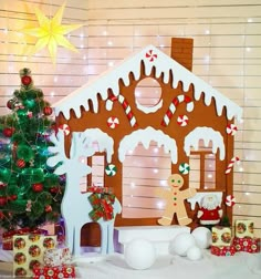 a gingerbread house with christmas decorations and presents around it on a white tablecloth