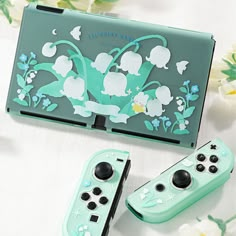 two nintendo wii game controllers sitting next to each other on a table with flowers in the background