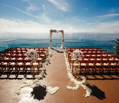 an outdoor wedding setup with chairs and flowers on the aisle, overlooking the ocean in clear blue skies