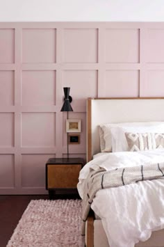 a white bed sitting next to a pink wall with lots of headboards on top of it