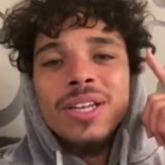 a man with curly hair wearing a hoodie pointing at the camera and making a peace sign