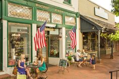 people sitting at tables in front of a store with american flags on the outside wall