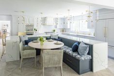 a kitchen and dining room with white cabinets, marble counter tops and blue cushions on the bench