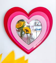 a pink heart shaped mirror with yellow flowers in it and a vase full of sunflowers