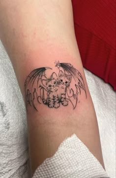 a small tattoo on the arm of a woman with a cat and bat design in black ink