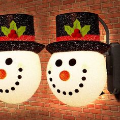 two snowmen with hats and holly leaves on their heads are attached to a brick wall