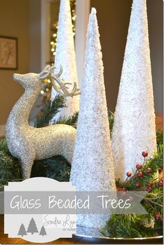 three white christmas trees sitting on top of a wooden table next to a silver deer