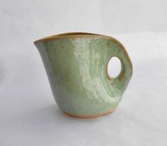 a small green cup sitting on top of a white table next to a vase with a hole in it