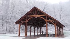 a covered pavilion in the middle of a snowy forest