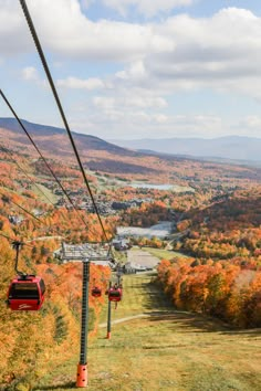 a red ski lift going up the side of a mountain with trees in fall colors