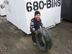 a young boy holding an old tire in front of a white box with writing on it