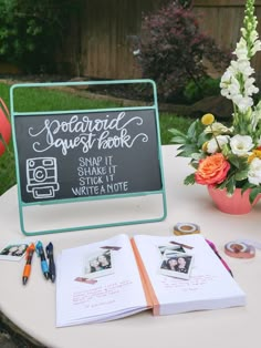 a table topped with an open book next to a flower pot and a chalkboard sign