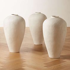 three white vases sitting on top of a wooden table