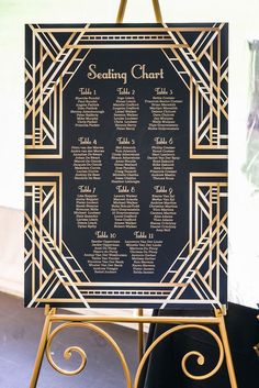 a black and gold wedding seating chart on a easel with purple border around it