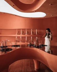 a woman standing in front of a counter with wine glasses on it and shelves filled with glassware