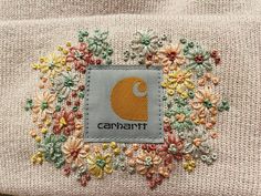 a close up of a patch on a sweater with flowers in the center and an embroidered logo that says canaant