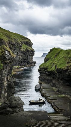 two small boats are in the water near some cliffs and grass on either side of them