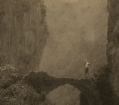 a man standing on top of a bridge over a river next to a tall cliff