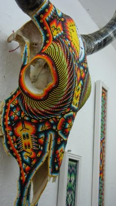 an animal sculpture hanging from the side of a white wall with colorful designs on it