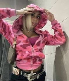 a woman with blonde hair wearing a pink hoodie and black shorts standing in front of a mirror