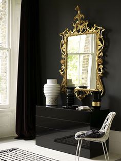 a black and white room with a gold framed mirror on the wall next to a chair