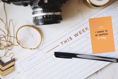 a desk with a notepad, camera and other items on it that says this week