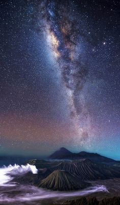 the night sky with many stars and clouds above some mountain tops, as seen from an island