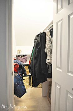 an open closet with clothes and bags hanging on the door handle, in front of a white wall