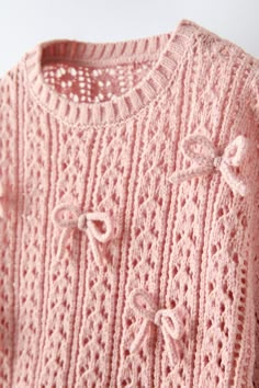 a pink knitted sweater with bows on the front and back, sitting on a white surface