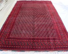 a large red rug sitting on top of a bed next to a white sheet covered floor