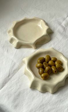 two bowls with olives in them on a white tableclothed surface, one bowl is shaped like a shell and the other is shaped like a fish